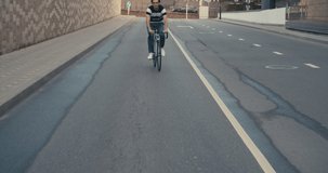 Young hipster man in casual summer cloths riding his fixed gear bike along the bike lane on city street. Front tracking shot young guy biking bicycle on road. 4K slow motion raw video footage 60 fps