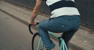 Young hipster young man in casual summer cloths riding his fixed gear bike along the bike lane on city street. Front tracking shot Side view Close-up of wheels. 4K slow motion raw video footage 60 fps