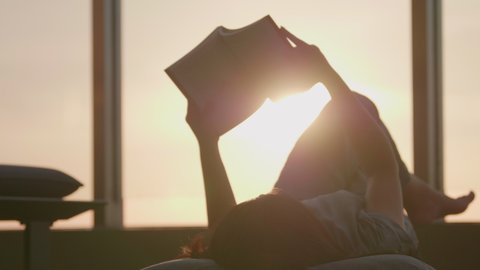Woman relaxed reading a book outdoors lying in a balcony on the beautiful sunset background. 
