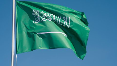 Flag of Saudi Arabia Lit by the Sun. The Big State Flag is illuminated by the sun and flutters epically in the wind against the blue sky. Slow Motion 240 fps