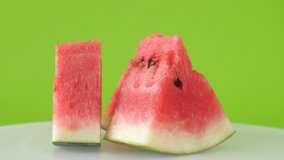 Close up slices of fresh red watermelon rotates on white plate with green background. Three pieces of watermelon. footage 4k
