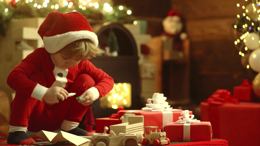Happy cute child in Santa hat with present have a Christmas. Happy little child dressed in winter clothing think about Santa near Christmas tree