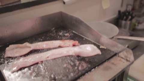 man flip the meat slices into cooking pan with use of food tong.