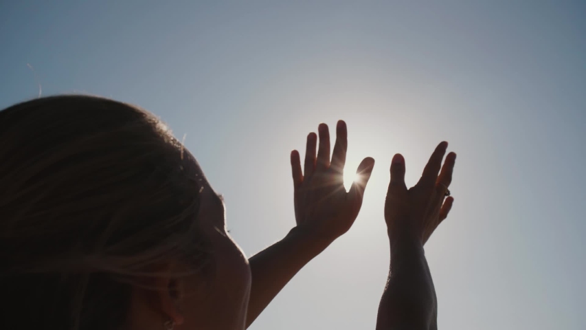 Beautiful young woman pulls her hands to the sun and plays with her fingers with sunrays. Hands silhouette with lens flare. Slow motion | Shutterstock HD Video #1032062915