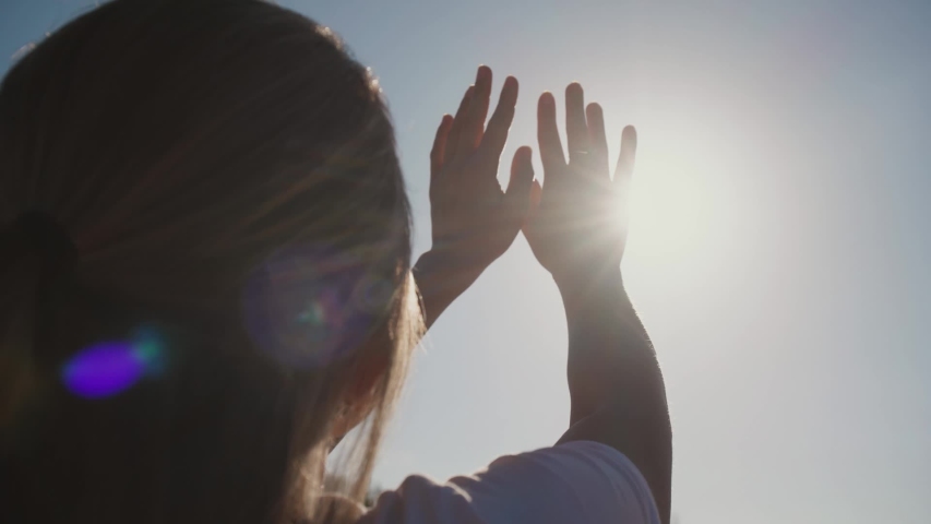 Beautiful young woman pulls her hands to the sun and plays with her fingers with sunrays. Hands silhouette with lens flare. Slow motion | Shutterstock HD Video #1032062918