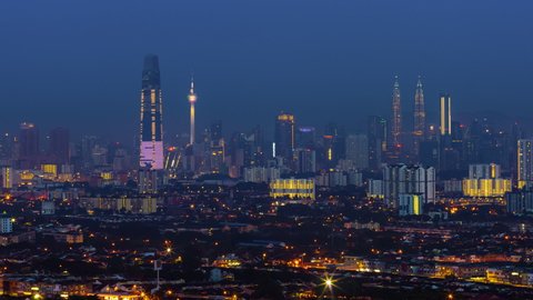 Time lapse: Kuala Lumpur City view during dawn overlooking the city skyline from afar as the first light hits the landscape at sunrise from night to day in Malaysia. Pan up motion timelapse.