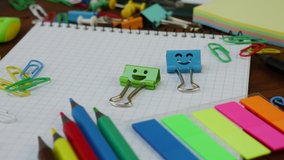 Smiles Blue and Green Binder Clips on Notebook with School Office Supplies: colored pencils and paper clips on brown wooden table. Concept of back to school and education