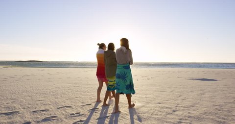 Three girl friends wrapped in towels keeping warm on windy beach