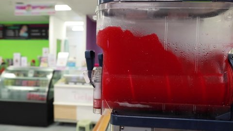 Pan close up shot of red slushy machine blending liquids
