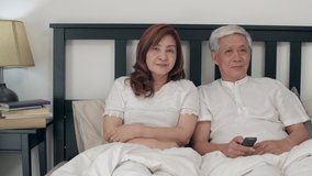Asian elderly couple watching television in bedroom at home, Asia couple enjoy love moment while lying on the bed when relaxed at house. Enjoying time lifestyle senior family concept. Slow motion shot