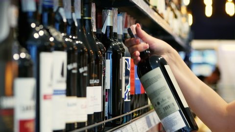 Woman chooses wine in the Supermarket, customer selects product on the shelves in the store in close-up Alcohol sale