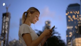 Cheerful female meloman listening positive song while typing text message via application on modern cellular phone, concept of millennial people and leisure time for hobby