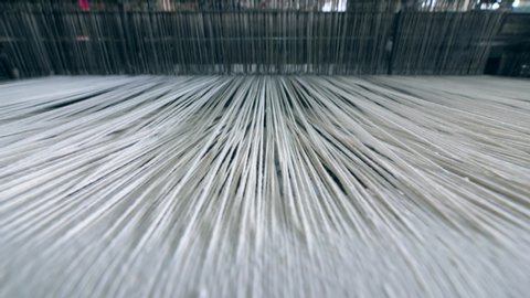 Industrial textile factory. Close up of thick white threads moving through the loom