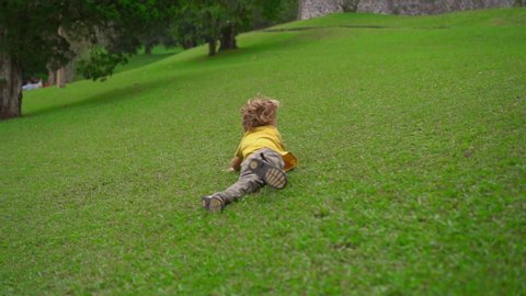 Superslowmotion shot of two little boys have fun on a lawn. They roll down the hill