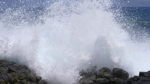 SLOW MOTION, CLOSE UP: Waves approaching the volcanic island crash into the rocky shore. Large swell coming from the Pacific Ocean splashing over the black volcanic rocks on the shore of Easter Island
