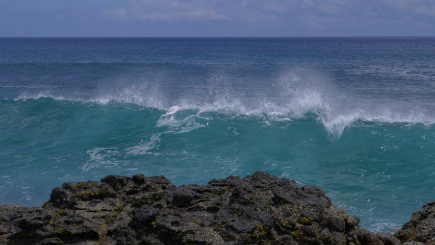 CLOSE UP: Big waves crash into the black volcanic rocks on the remote shore of Easter Island. Cinematic shot of a deep blue ocean swell violently splashing over the rocky coast of an exotic island. Royalty-Free Stock Footage #1032113483