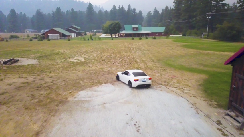 White sports car drifting in open field with aerial drone
