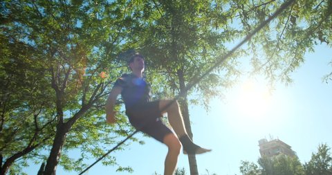 Young man performing as acrobat and training with slackline outdoors. Athlete doing sport activity and exercising with trickline in city park. Slow motion