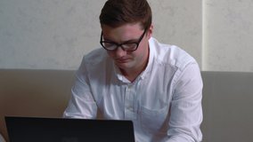 Young businessman interrupted by a mobile phone call as he sits working at a laptop computer pausing to answer it