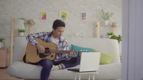 a young Asian man learns to play the guitar depends on the laptop training video