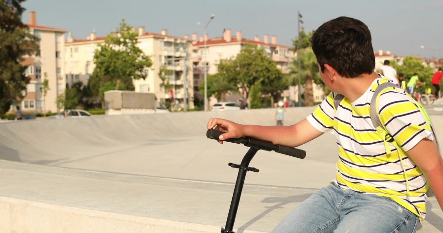 Handsome unhappy preteen boy with scooter sitting alone at the skateboard park Royalty-Free Stock Footage #1032126944