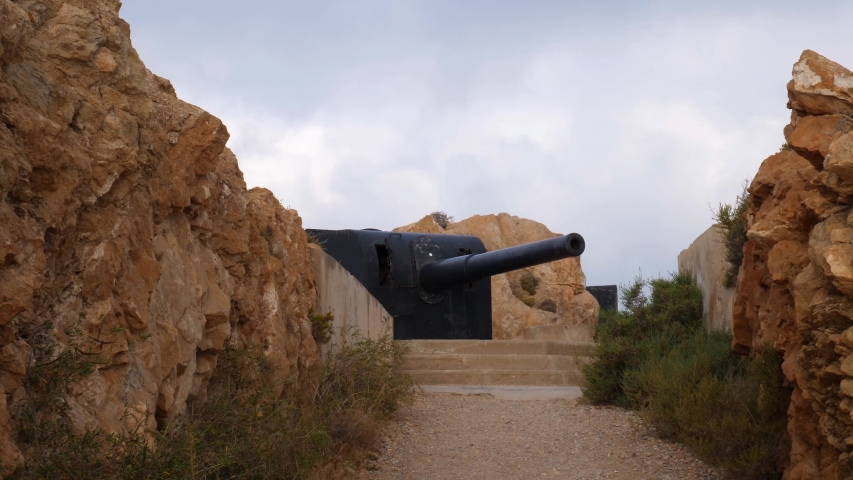 Mountain hiker looks at an old gun at the historic Spanish defenses Cabo Tinoso. He looks at the cannon and then at the sea. It is cloudy in the early morning.