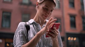 Slow motion effect of young hipster girl in headphones listening favourite music songs via smartphone application and writing text for funny publication on travel website