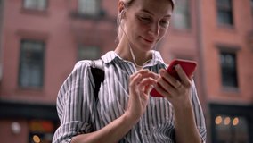 Slow motion effect of positive hipster girl searching audio books via free smartphone application for listening on leisure via electronic headphones, concept of millennial people