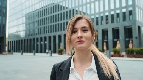 Portrait of young business woman in suit with blonde hair standing on the urban business district street. Skyscraper background. Business, finance, banking. Girl looking at camera.
