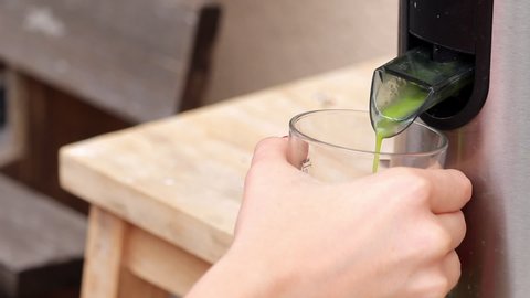 Close Up Hand Holding Glass Under Vegetable Juicer, Green Healthy Juice Dispenser