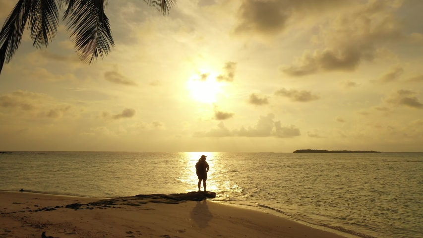 A silhouette of a woman is staying at the beach in front of the setting sun. Golden light on that tropical island Bali.