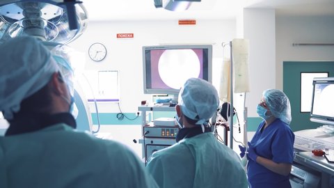 Doctors and a nurse are looking at endoscope monitor during surgical operation. Back view of a group of surgeons in medical uniform in operating room looking on a modern monitor.