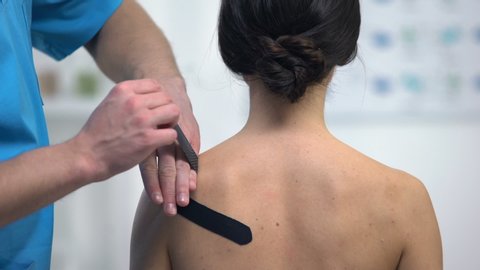 Physiotherapist applying Y-shaped tapes on female patient shoulder muscle strain