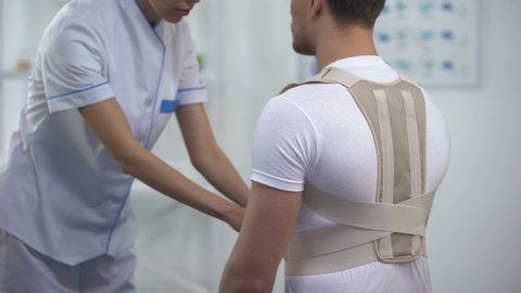 Orthopedist applying posture control shoulder brace male patient, healthcare