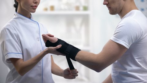 Professional orthopedist fixing wrist support pleased male patient, healthcare