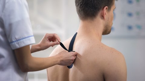 Experienced doctor applying Y-shaped tapes on patient upper back, healthcare