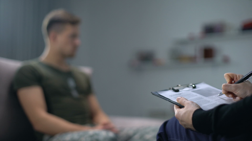 Psychologist making notes during therapy session with sad male soldier, PTSD | Shutterstock HD Video #1032161141