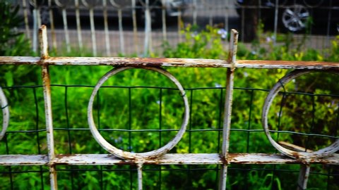 Rusty metal railing with a geometric design and folded in the center with green plants in the background