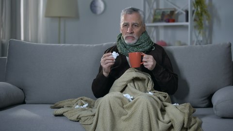 Ill pensioner sneezing and drinking hot beverage, treating influenza, flu season