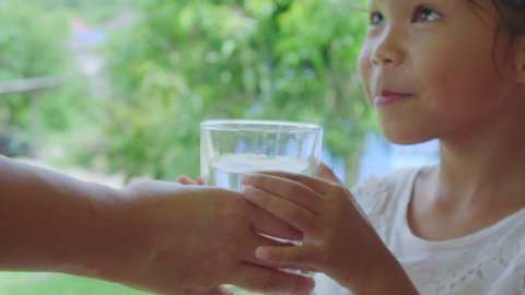 Close up shot of clean pure water glass while mother holding and gives to daughter drink in garden background, slow motion