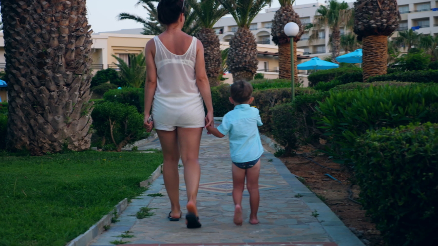 A woman and her son walk to a hotel from a beach.