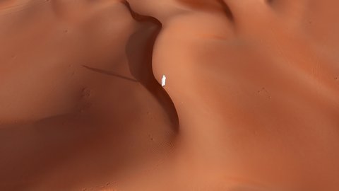 Arab man in traditional outfit walks on desert sand dunes. Middle east man in white clothing aerial view from above.