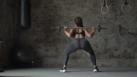 Back view of woman in black sportswear holding bar making weight-lifting exercise on the background of a brick wall