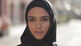 Portrait of beautiful young Muslim woman wearing hijab headscarf looking into the camera standing on the old city background.
