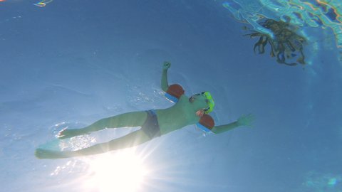 Underwater footage of a boy swimming in a pool, wearing armbands.