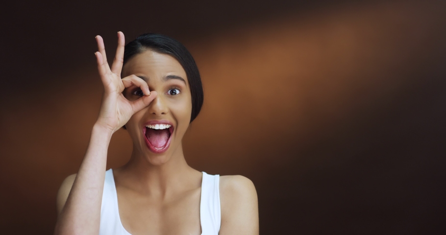 Close up of the cheerful young Caucasian beautiful girl laughing ang having fun to the camera on the brown background. Portrait.