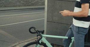 people, style, technology, leisure and lifestyle - happy young hipster man with smartphone and fixed gear bike on city street 4K slow motion raw video footage 60 fps