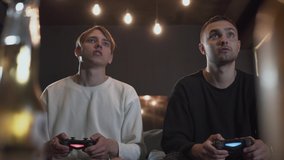 Two happy friends playing video game in the gaming room sitting on the sofa. Friends spending time together indoors. Video game and leisure concept.
