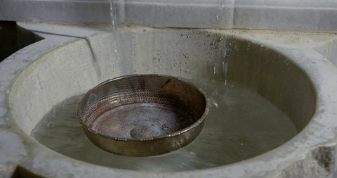 ancient bowl is floating on water surface in small stone washbasin, close-up view