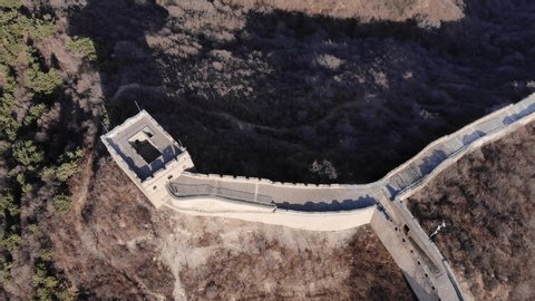 Top down aerial view of watchtower at sharp turn of Great Wall of China. Typical fortification from stone bricks at hill summit, camera soar over while tilt down
